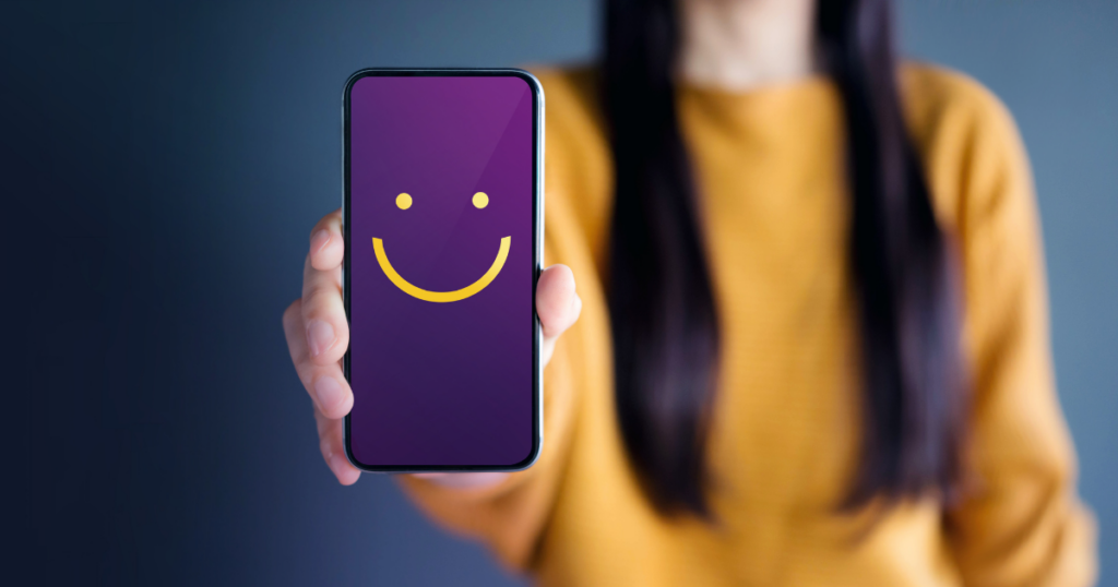 A woman holding a smartphone with a smiley face on it.